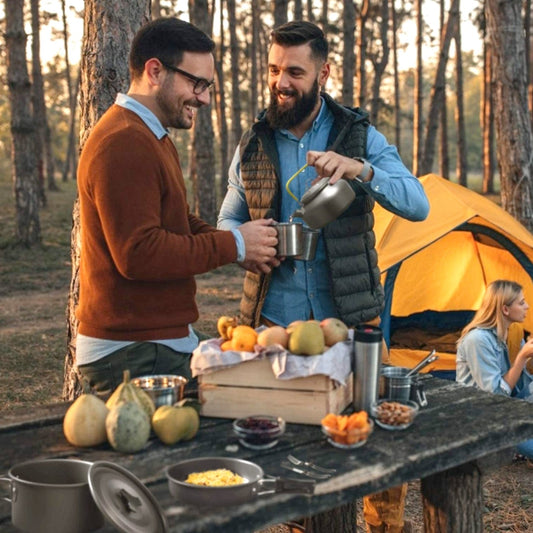 Two men pouring hot drink from kettle at forest campsite