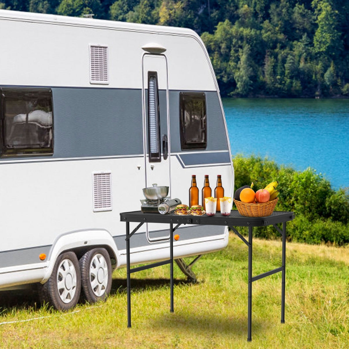Folding camping table outside camper near lake with food and drinks