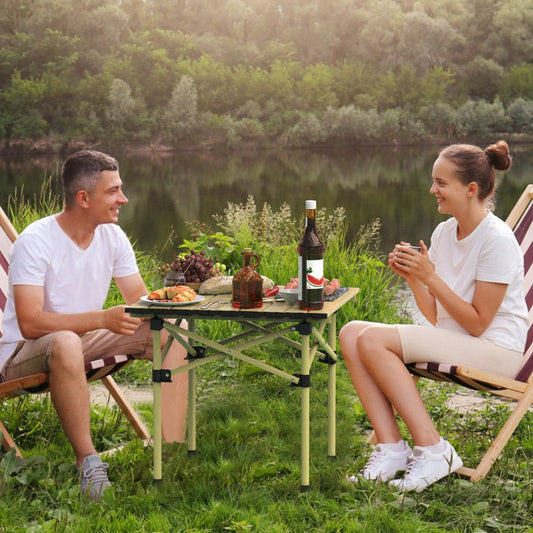 Folding camping table set between two chairs beside a lake with food on top