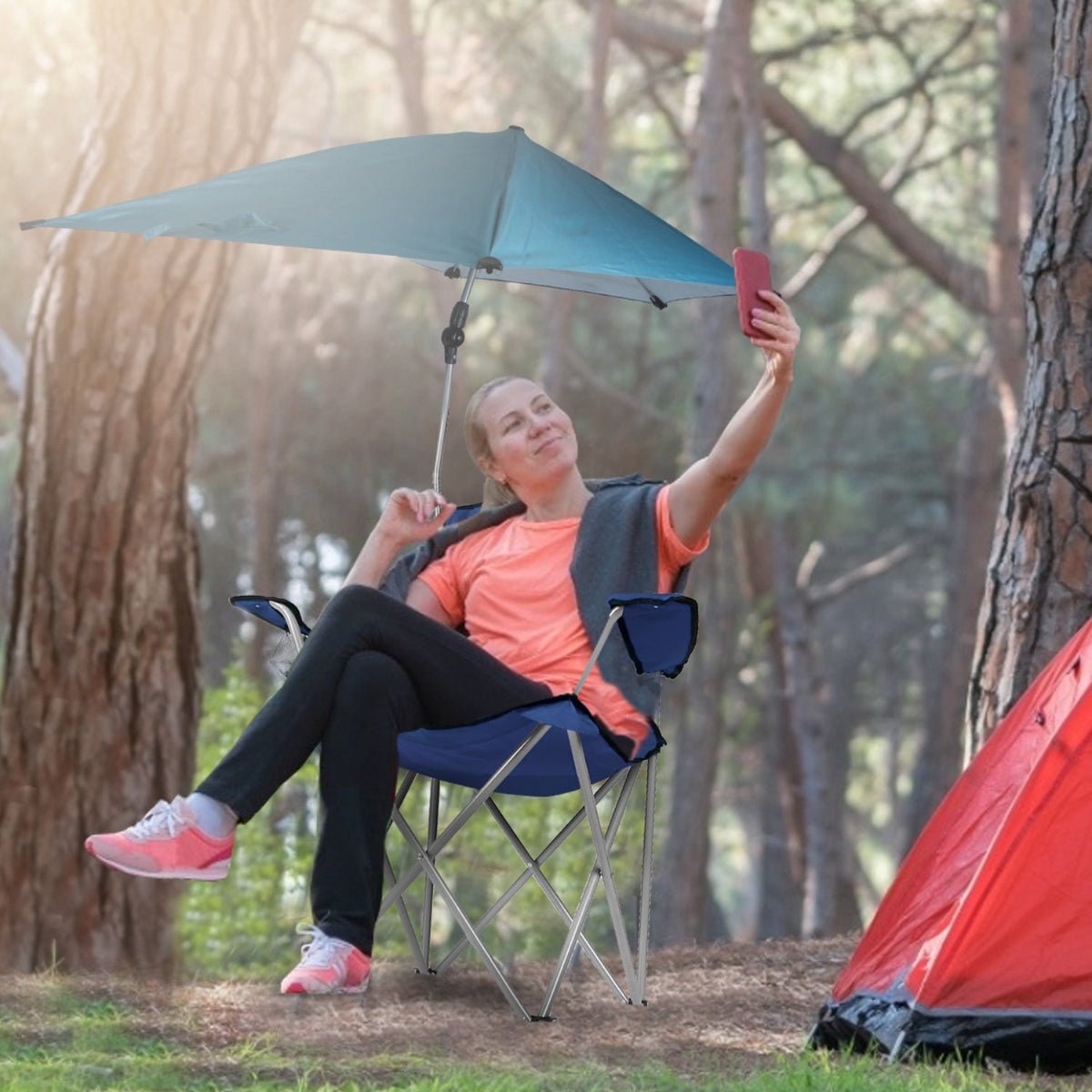 Person sitting in folding camp chair with umbrella near a tent