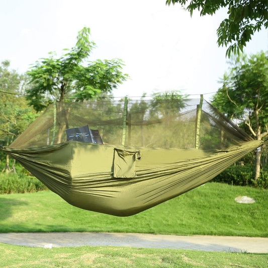 Camping hammock with mosquito net suspended between trees in grassy outdoor setting