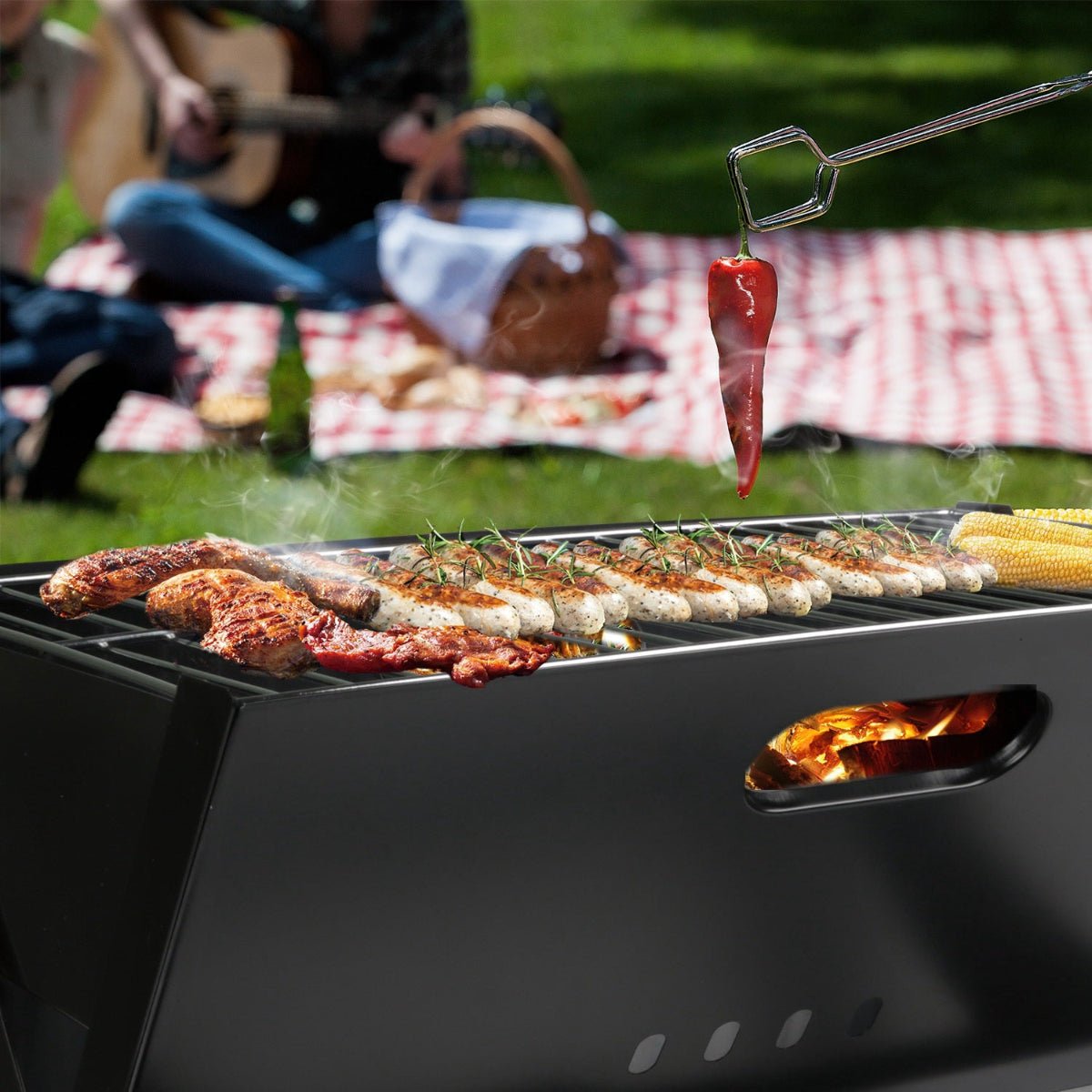 Foldable charcoal grill cooking sausages and meat at an outdoor picnic setting