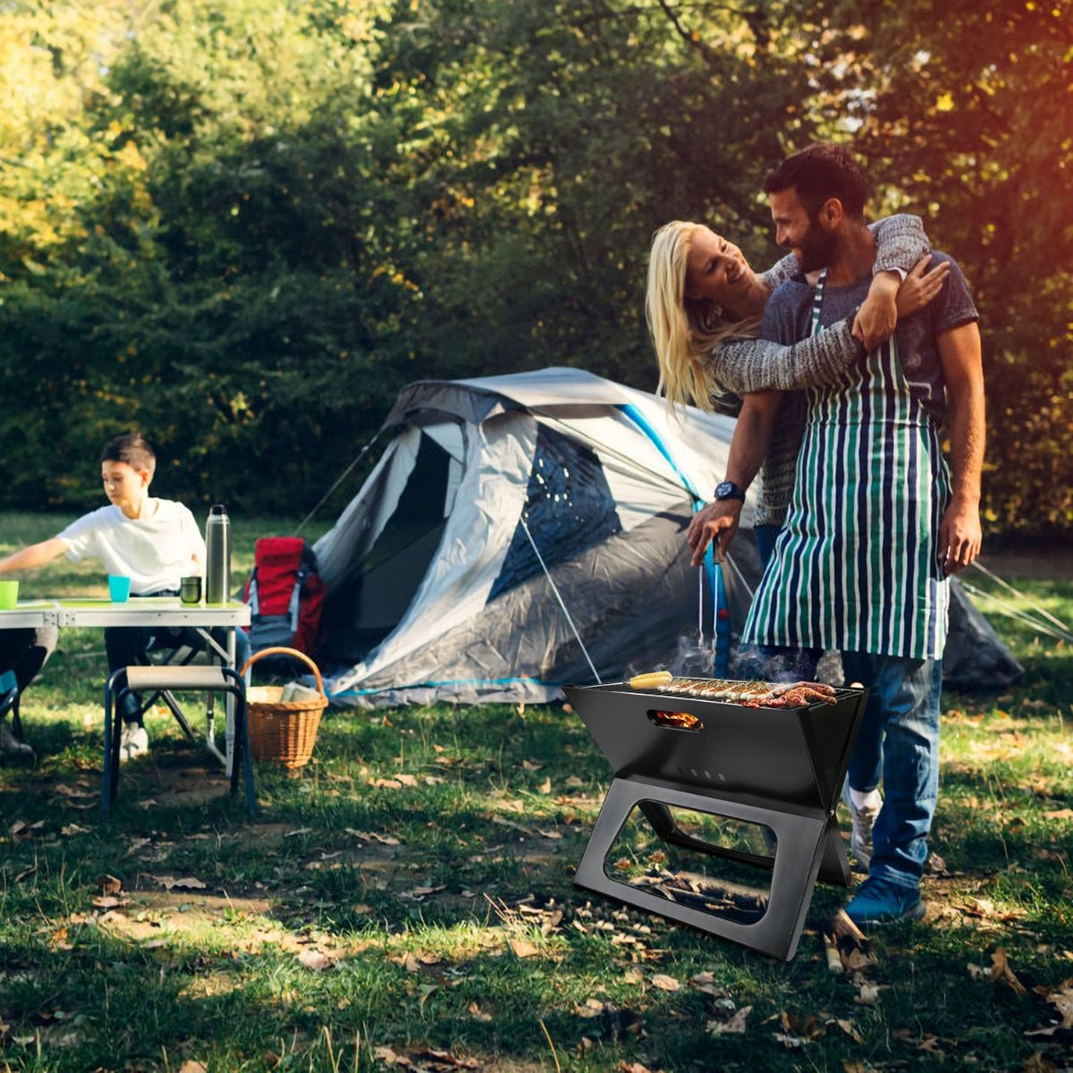 Compact charcoal grill in use beside a tent at a wooded campsite