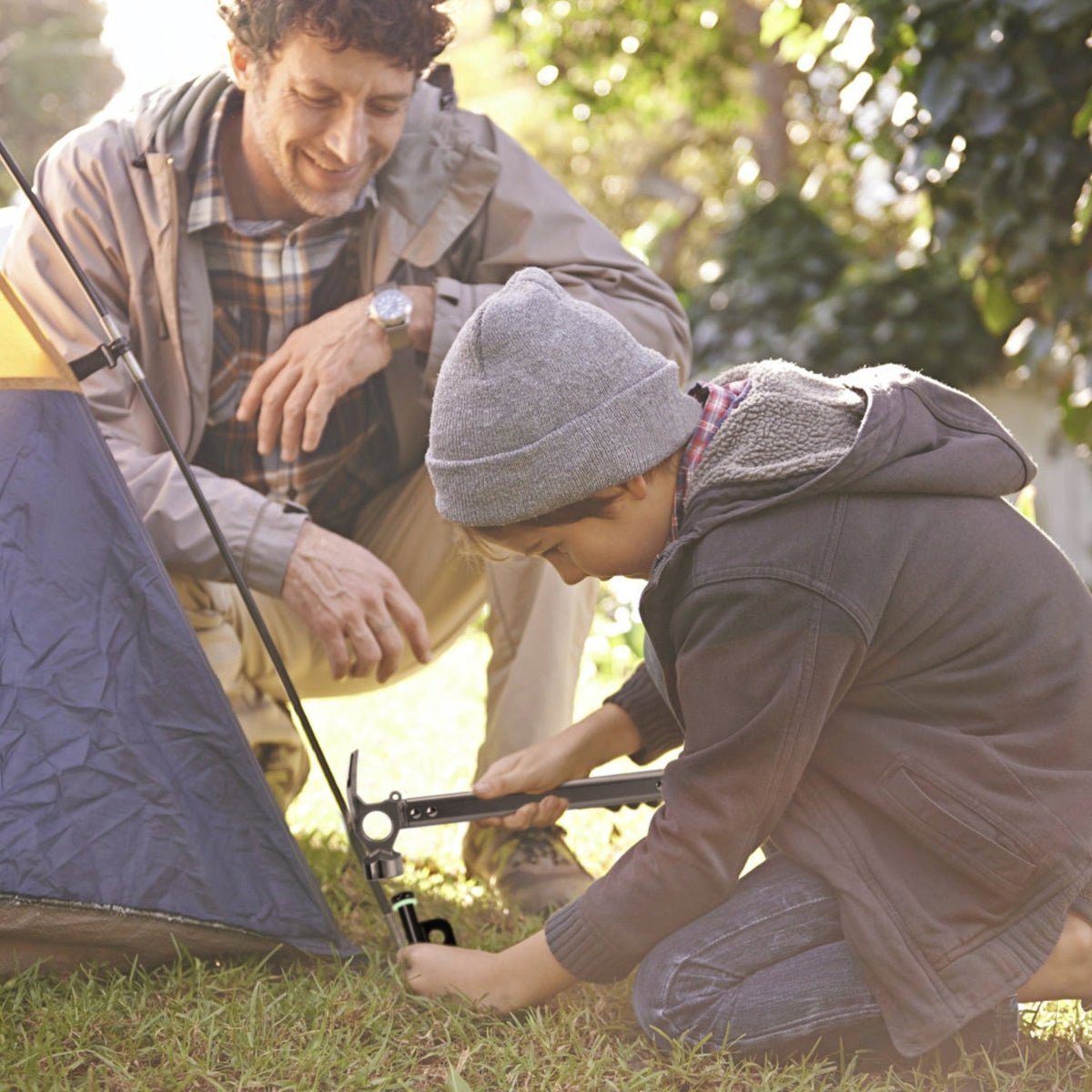 Person securing a tent stake with hammer beside a pitched tent outdoors